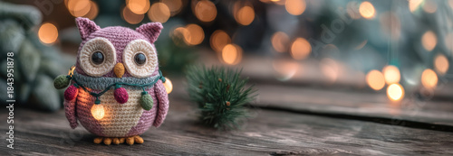 Crocheted pink owl wrapped in colorful holiday lights sits on rustic wood with bokeh lights..Perfect for cozy Christmas marketing, DIY craft features, or festive toy promotions.