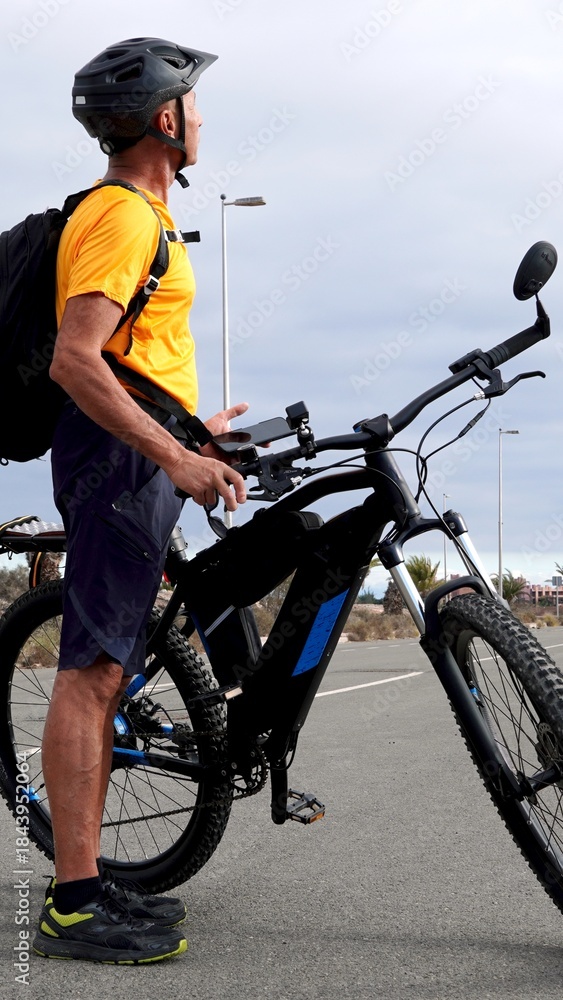 Fototapeta premium Active man cycling an electric mountain bike, dressed in sportswear and helmet, enjoying a healthy lifestyle and outdoor activity under a spring sky in the Canary Islands