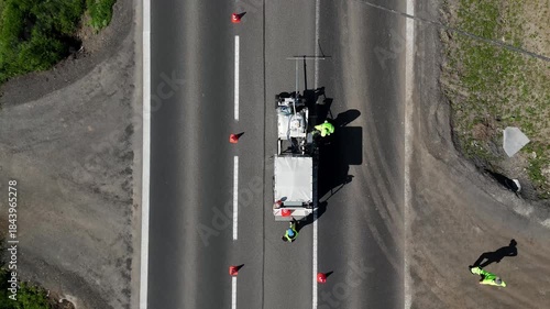 Drone top view of road workers applying lane markings on asphalt, showing infrastructure maintenance, traffic safety work, and organized urban road improvement.