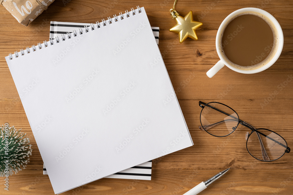 Obraz premium A cozy holiday desk setup featuring a blank notebook, glasses, a warm cup of coffee, and festive decorations ready for note taking, planning, or creative writing during Christmas and New Year
