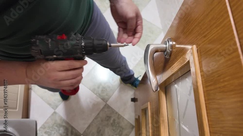 Handyman repairing wooden door handle with power screwdriver
