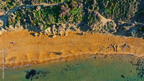 Drone top sunset view of sand beach, people, green hills. Ghain Tuffieha, Malta island