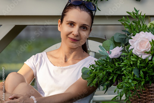 portrait of a young beautiful brunette woman in a summer park in a white shirt with rose flowers