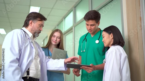Medical team discussing patient data on tablet in hospital hallway.