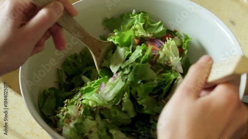 Slow motion video of a fresh salad being gently mixed and tossed using a wooden spoon

