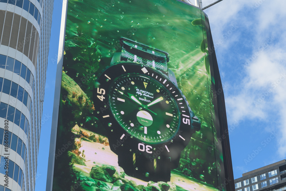Naklejka premium close-up of digital advertisement featuring Swatch x Blancpain collaboration (Blancpain’s iconic Fifty Fathoms) dive watch facing Sankofa Square, Toronto