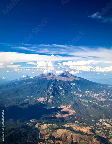 Aerial shot of towering mountains under a vibrant blue sky with fluffy white clouds, and green valleys