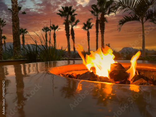 Glowing natural gas fire pit plus ceramic rocks with palm trees and mountains during lovely sunset