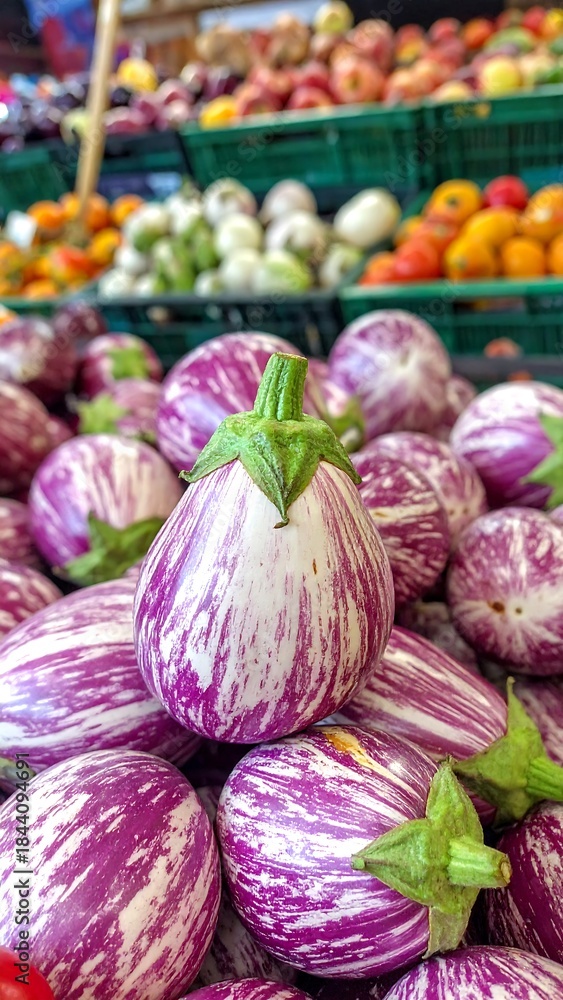 Fototapeta premium Fresh, striped eggplants stacked at a farmers market, other produce blurred in background