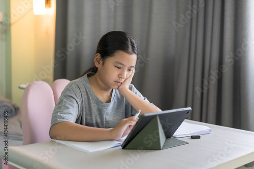 asian child study online class to bored learning on computer tablet or kid girl student sleepy sits hand on chin to studying or young people learn from home school by video call technology education