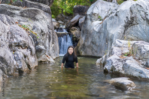asian child playing waterfall or kid girl happy smile standing in natural pond water with rocks stones or young people in nature stream in summer and forest for holiday travel adventure at lan sang