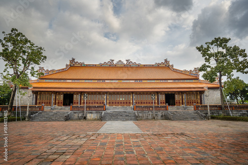 Imperial Palace in Hue, Vietnam, showcasing Grand Traditional Architecture with an Ornate Orange Tiled Roof under a Cloudy Sky.