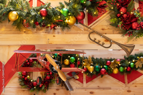 A festive Christmas display features lush garlands, colorful ornaments, and a wooden airplane toy on a rustic shelf, creating warm, welcoming holiday decor for family gatherings and seasonal marketing