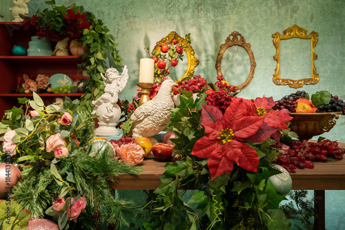 Lush indoor floral scene featuring poinsettias, roses, and greenery on a wooden table, surrounded by decorative frames, a candle, and seasonal accents for warm and festive home decor