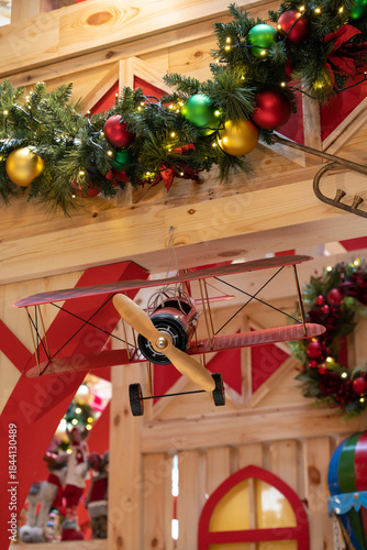 A warm holiday scene featuring garlands and colorful ornaments draped over a rustic wooden framework, with a playful toy airplane as a focal point, evoking family joy and cozy Christmas vibes.