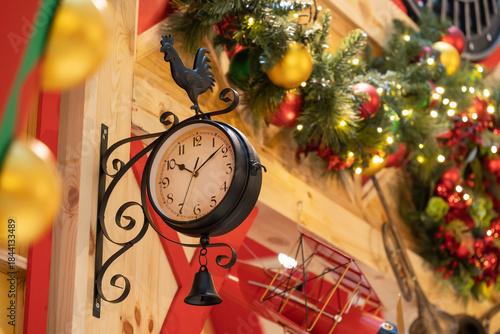 A charming vintage clock mounted on a wooden wall, featuring a rooster weather vane and a hanging bell. Surrounded by festive Christmas decorations and rustic decor creating a cozy holiday.