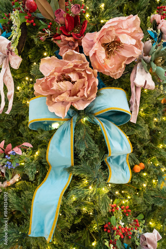 A festive Christmas tree adorned with lush greenery, soft pink roses, and a bold turquoise ribbon bow.