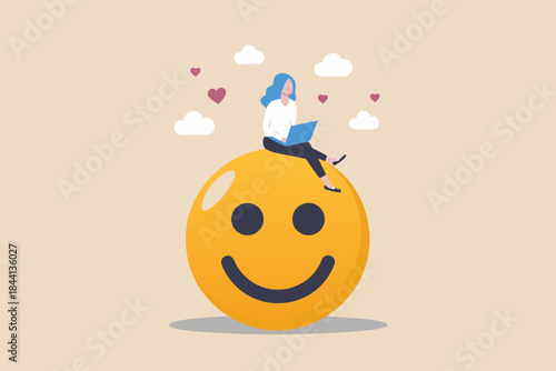 Woman working on laptop perched atop a giant smiling yellow emoji