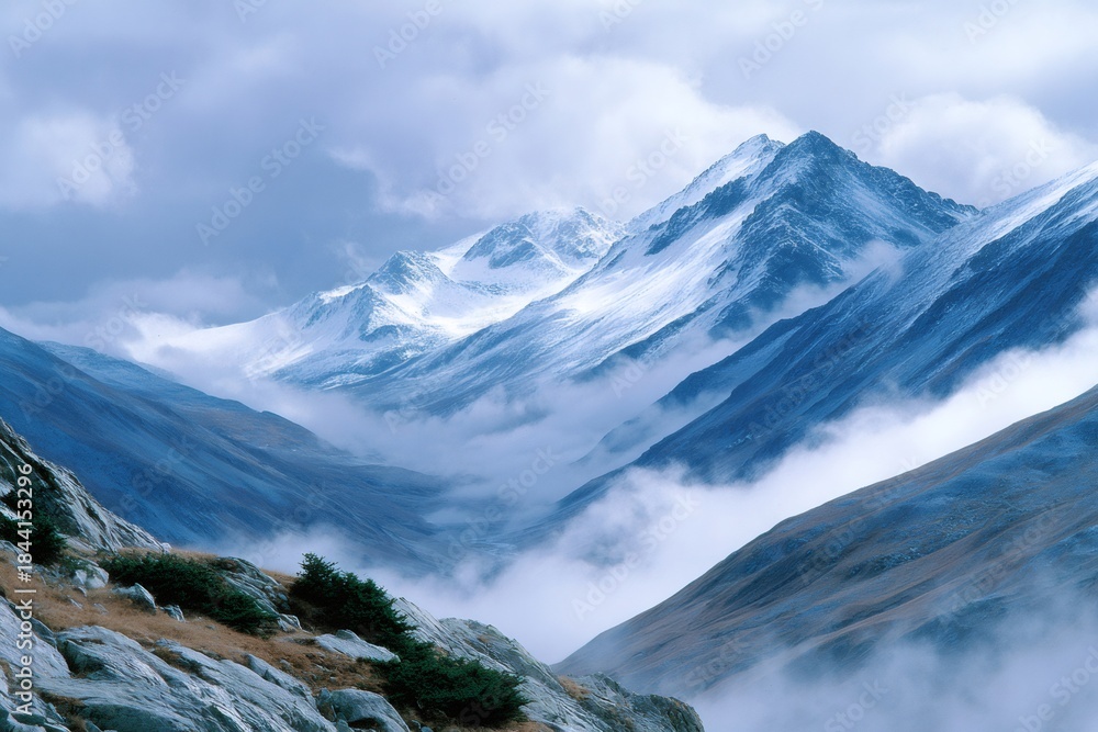 Fototapeta premium Snowcapped mountains with valley shrouded in mist and clouds