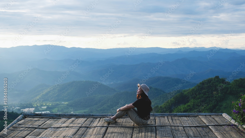 Obraz premium A woman sitting on wooden terrace and looking at a mountain view before sunset