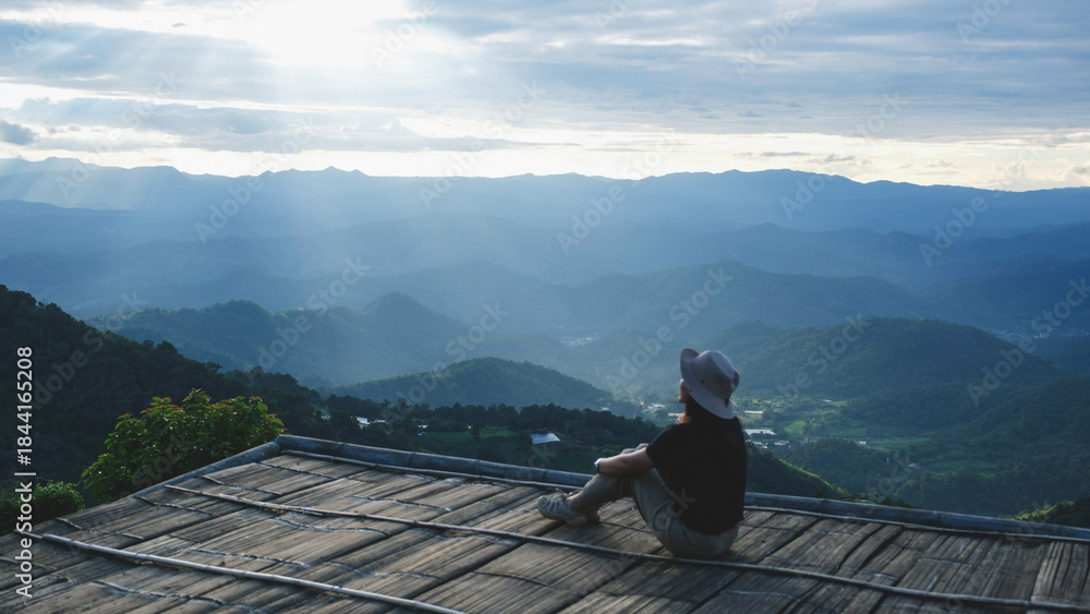 Obraz premium A woman sitting on wooden terrace and looking at a mountain view before sunset