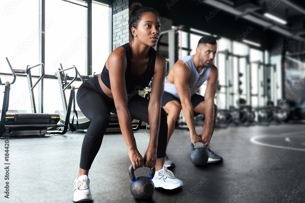 Fototapeta premium Fit and muscular couple focused on lifting a dumbbell during an exercise class in a gym.