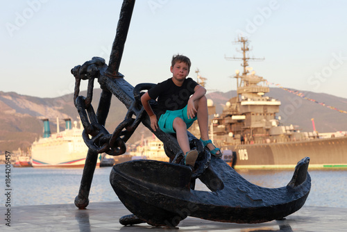 Small boy sitting on anchor at port
