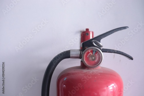 Close-up of a red fire extinguisher mounted on a white wall, showing its gauge and handle.