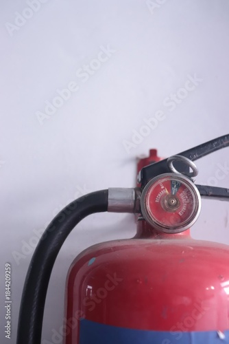 Close-up of a red fire extinguisher with a pressure gauge against a white wall.