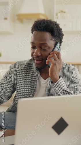 Multitasking male freelancer talking by phone and working with laptop at home workplace. Vertical portrait of businessman or office worker in distance mode, online job for web-developer or designer
