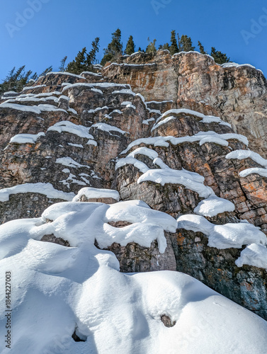 Winter snowy rocks with fir trees - winter background. Nature details during a walk in the mountains - winter activities in Rocky Mountains