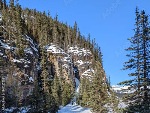 Winter in the mountains - frozen lake, snow-covered rocks, spruce trees covered with snow on a sunny day - winter vacation - snowshoe hiking and ski trails, Lake Louise, Alberta, Canada