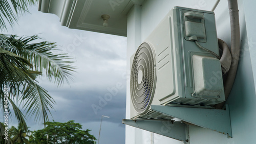 Outdoor Air Conditioner Compressor Unit Against White Wall with Cloudy Sky