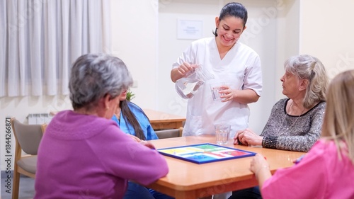 Caregiver serving water to senior women playing board game