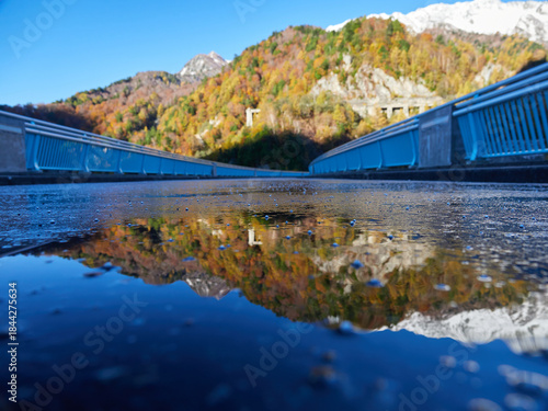 秋の観光名所立山黒部アルペンルートの黒部ダムの貯め水に映すカラフルな紅葉と初雪の雪山の風景