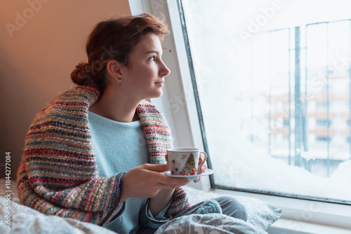 young woman warms up with hot tea in winter weather at home