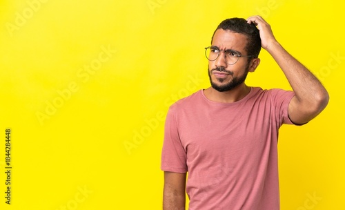 Принти на полотні Young latin man isolated on yellow background having doubts while scratching hea