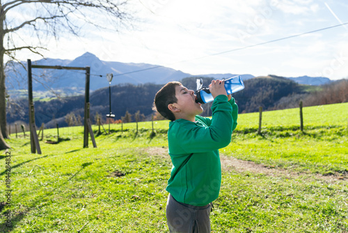 Billede på lærred Boy drinking water from a plastic bottle, staying hydrated during outdoor activi