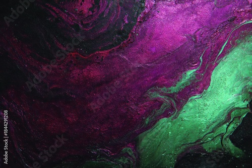 Swirls of purple and green paint blend together on a canvas creating an abstract design in a studio