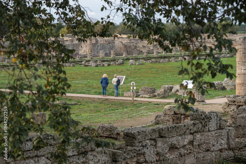 Tourists exploring ancient ruins of Paestum while reading archaeological infopoint