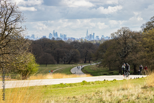 Canvas Print Cyclists riding uphill through a London park with city skyline in the distance