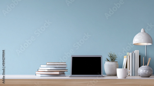 Organized workspace featuring a laptop books plant lamp and mug against a blue backdrop