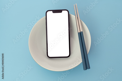 A modern smartphone with a blank white screen and a pair chopsticks on a bowl; calculate daily nutrition intake with smartphone technology