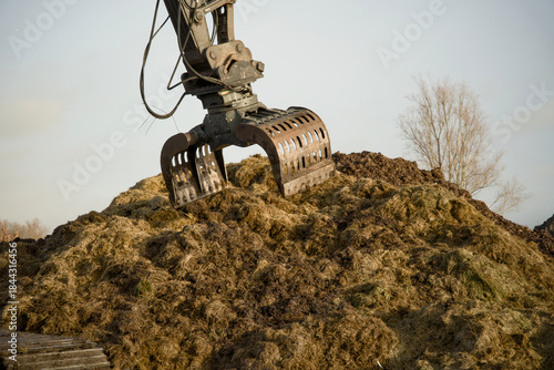 Excavator digging into a large pile of green waste during the composting and bokashi process. The machinery processes organic residual streams to produce peat-free substrate for sustainable horticultu