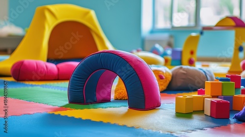 Colorful soft play tunnel arch in a bright indoor children's playroom with various toys and equipment