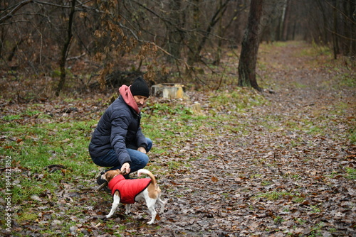 Man enjoys a walk with his dog on a muddy trail in a quiet forest during a cool, overcast day