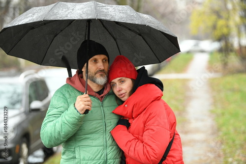 Couple shares an umbrella while walking in the rain on a chilly day in the park