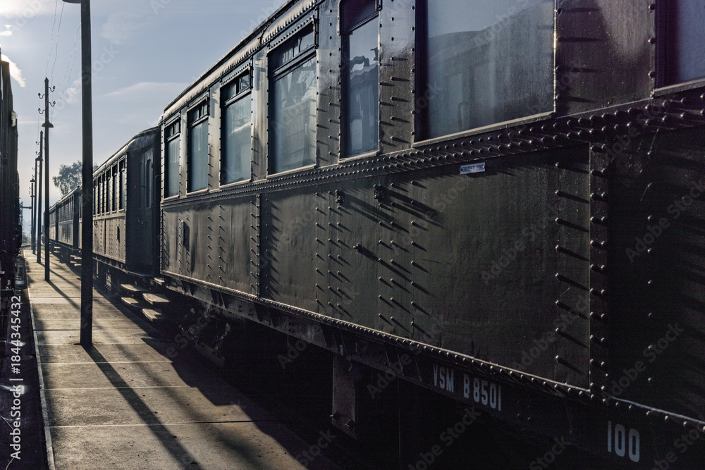 Obraz premium Perspective view of vintage dark green riveted passenger train carriages parked at the platform during a sunny day at the railway museum.