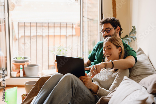 Billede på lærred Man puts his arm around woman and points at laptop she holds on her lap while th