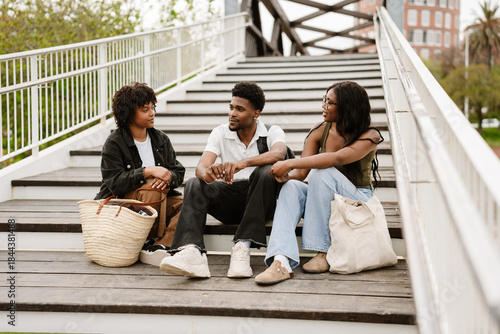Foto A group of three friends sit on the steps of a bridge while one of them talks an